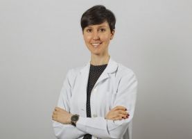 Una mujer con una bata de laboratorio blanca está de pie con los brazos cruzados y sonriendo.